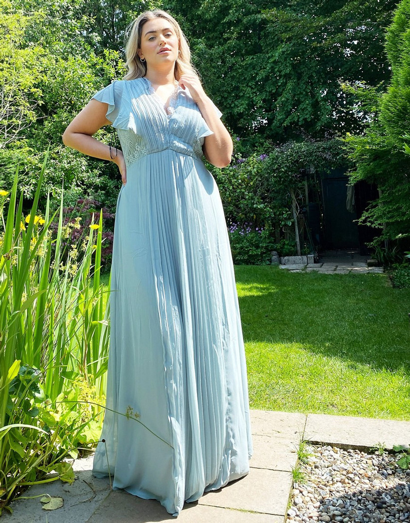 Model in garden wearing pastel blue bridesmaid dress with pleats and ruffled short sleeves