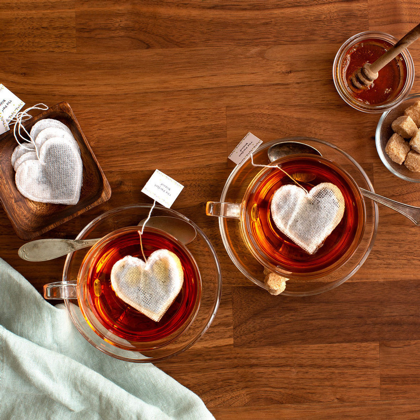 Two glass mugs of tea with heart-shaped tea bags brewing small Valentine's gift idea