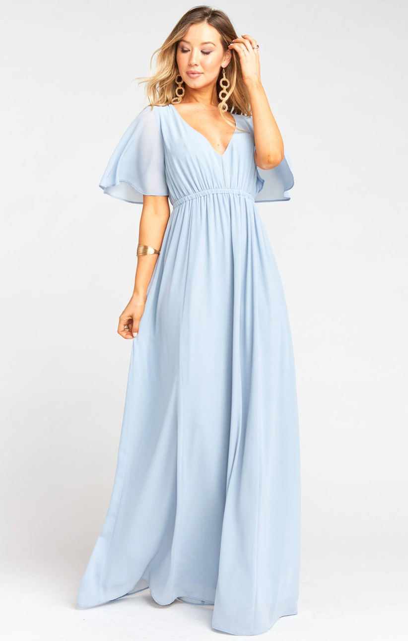 Model wearing pastel blue bridesmaid dress with empire waist and cape sleeves