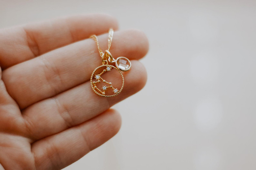 Gold constellation zodiac necklace with birthstone in a person's hand