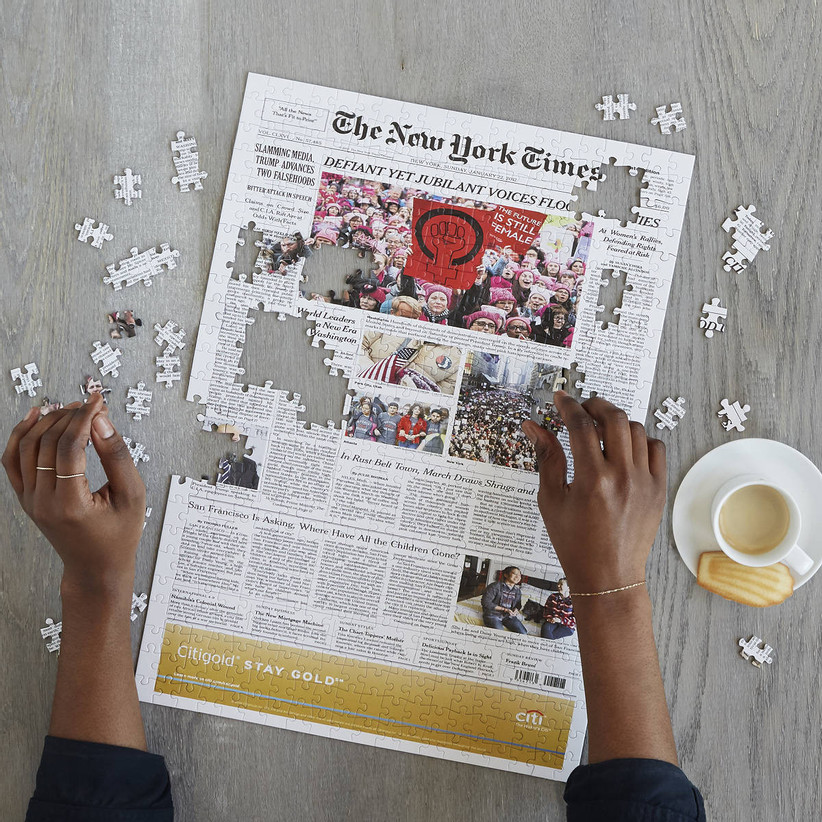 Woman's hands completing custom puzzle of New York Times front page