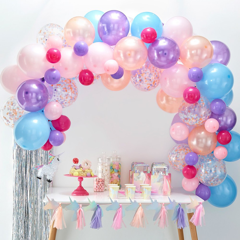 Pretty balloon garland arch in pastel hues of pink, blue, and purple arranged over a dessert table