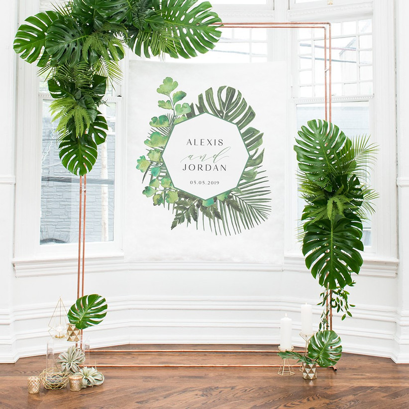 Tropical bridal shower backdrop personalized with couple's names and the date set up in light, airy room