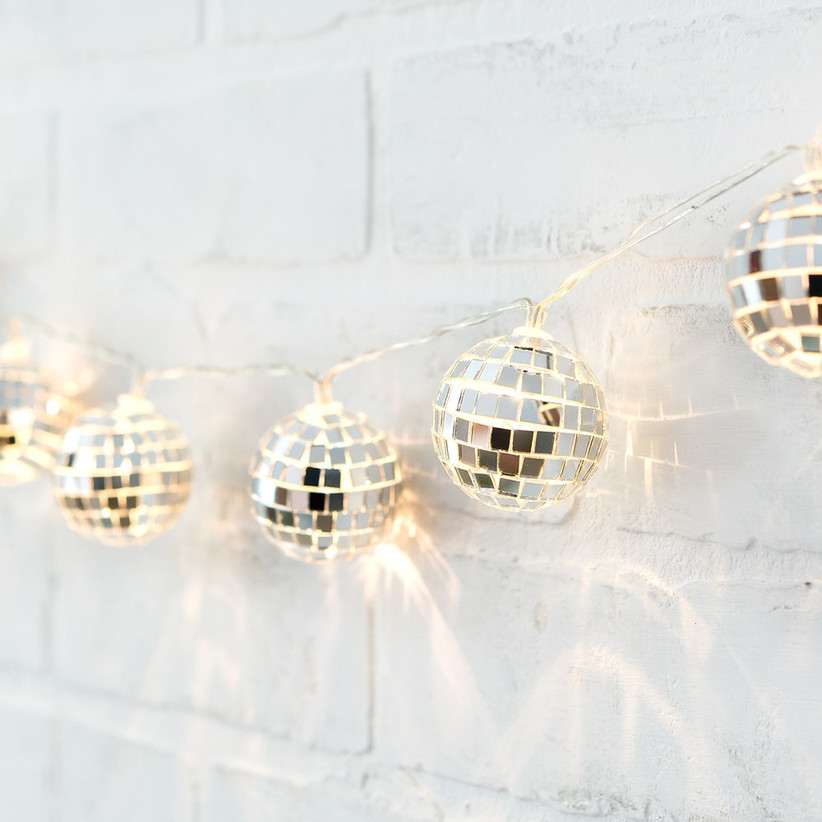 Close-up of disco ball string lights draped on white brick wall
