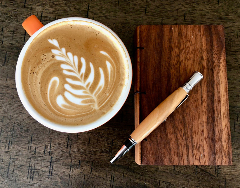 Wooden willow pen pictured next to a cup of coffee on top of a notebook