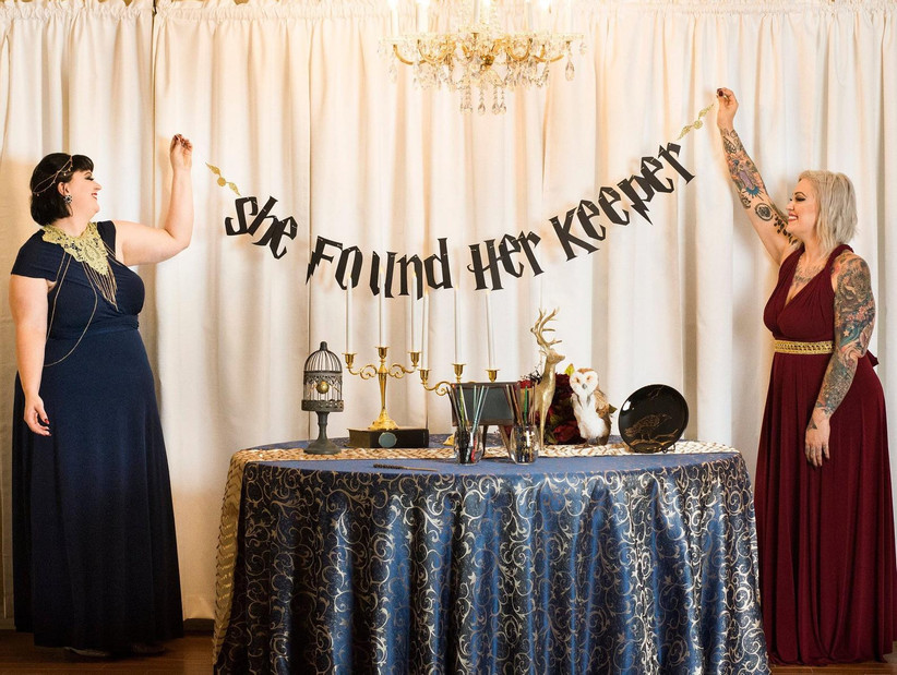 Two women holding up a bachelorette party banner that reads: She found her keeper