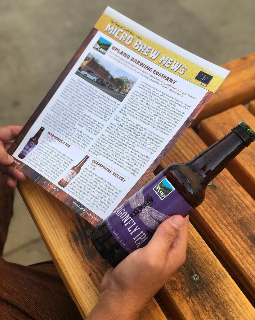 Close up of man holding bottle of craft beer in one hand and Beer Club newsletter in the other