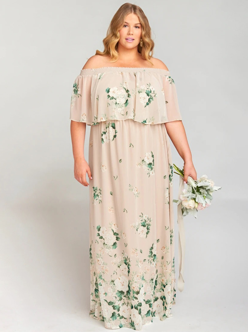 Plus-size model wearing blush pink off-the-shoulder bridesmaid dress with ruffled bodice and white and green florals
