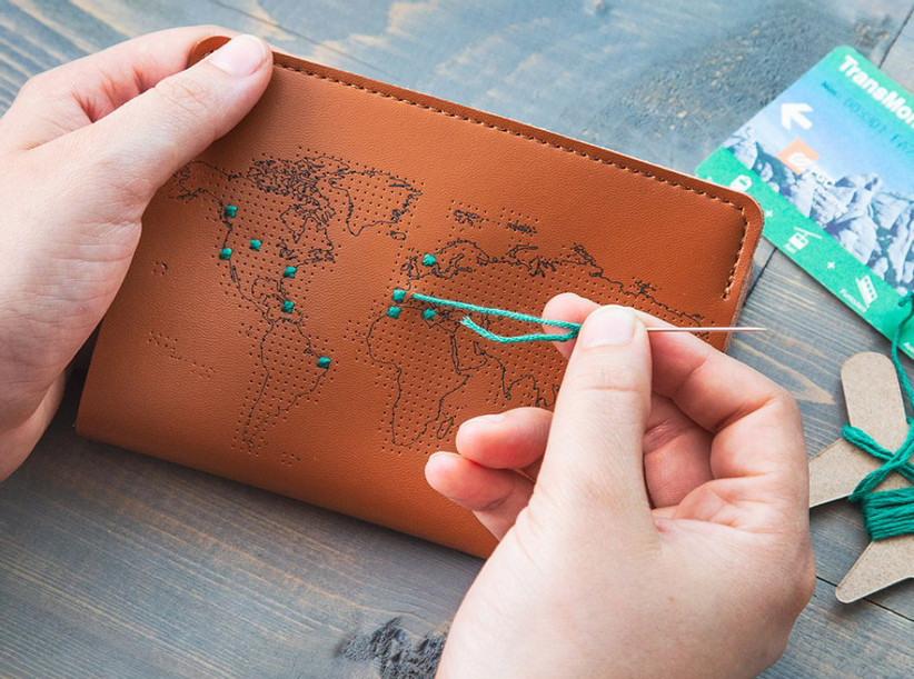 Person stitching a thread into map passport cover to mark travels