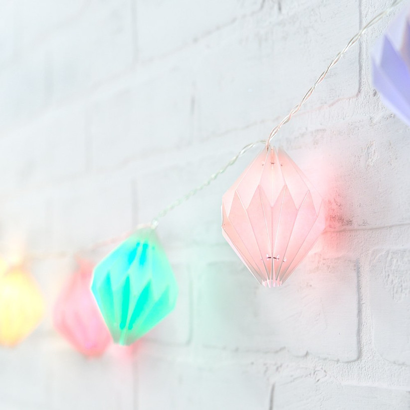 Close-up of pastel paper lantern string lights on white brick wall