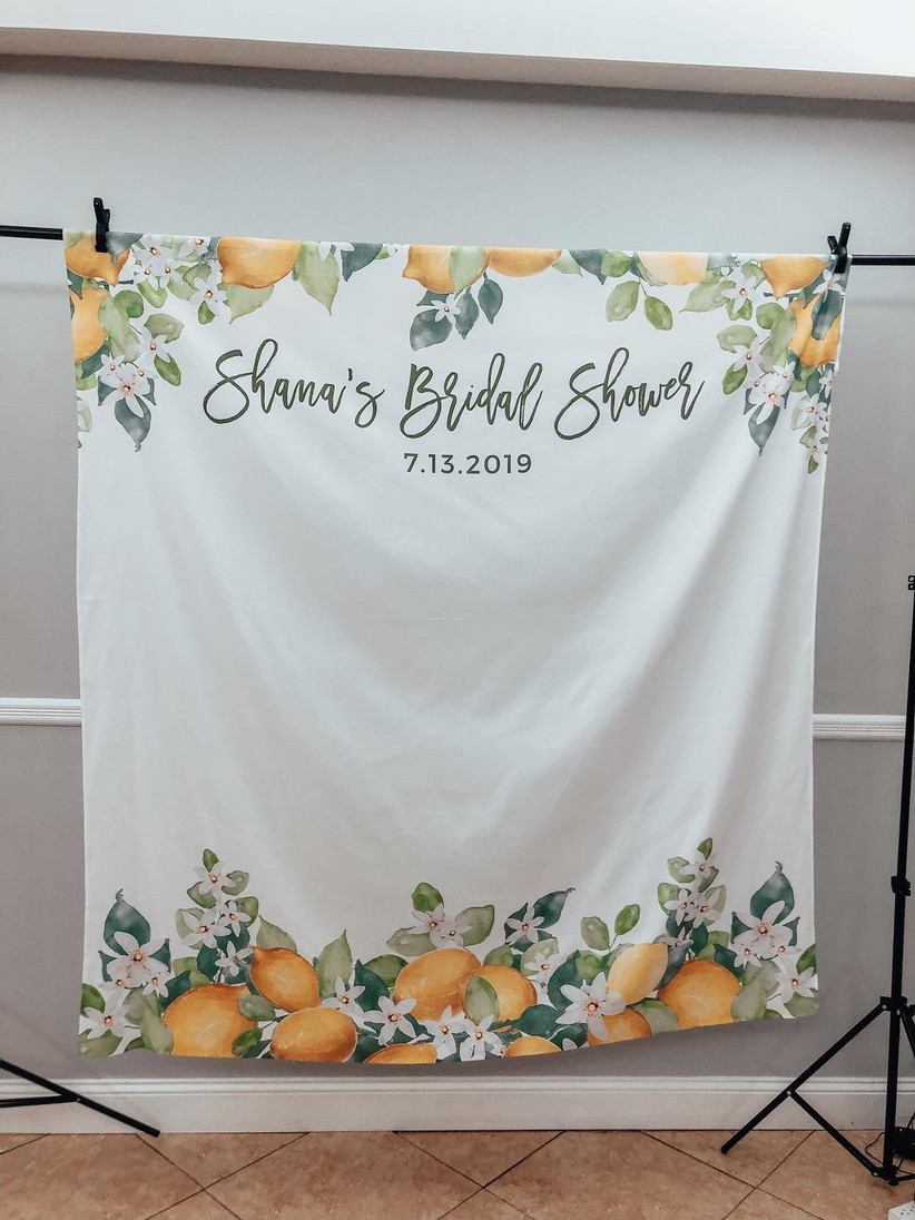 White bridal shower backdrop with lemon and greenery motif border