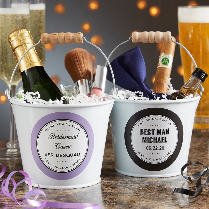 Two cute metal buckets personalized with bridesmaid's name and wedding title and best man's name and wedding title with different things inside such as mini champagne and a bowtie