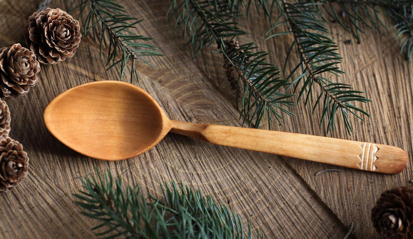 Wooden serving spoon made from willow surrounded by pine cones and spruce leaves