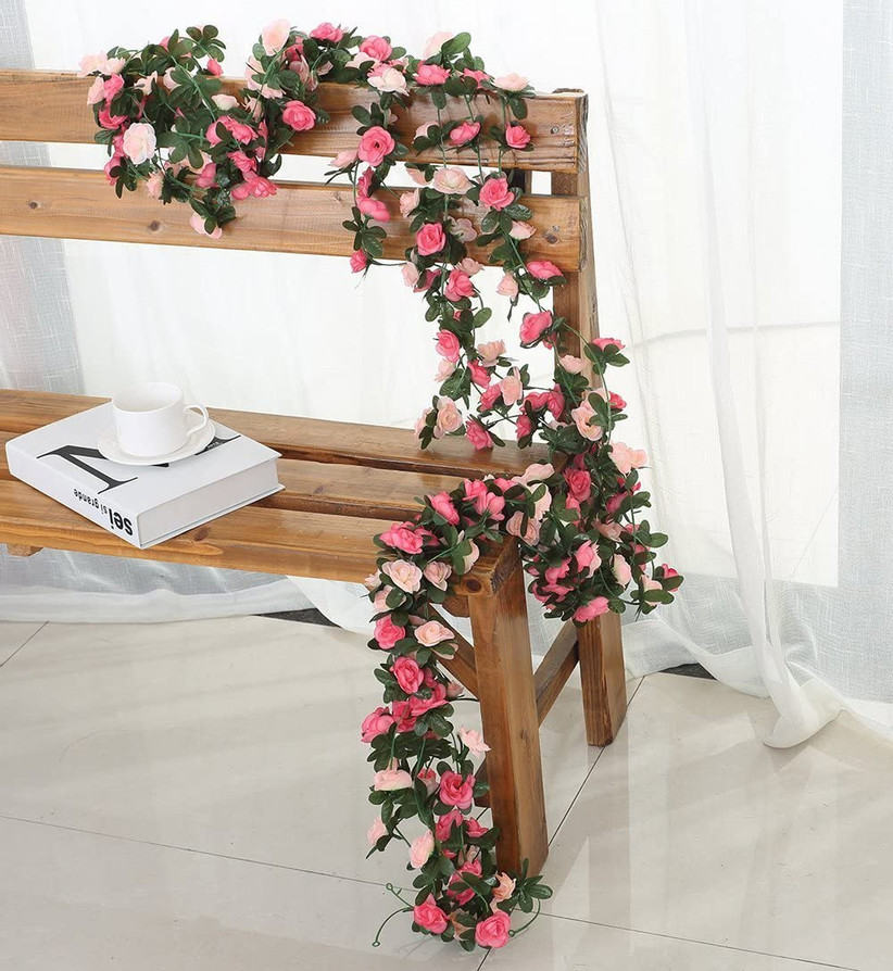 Artificial greenery and pink floral garland draped over a wooden bench