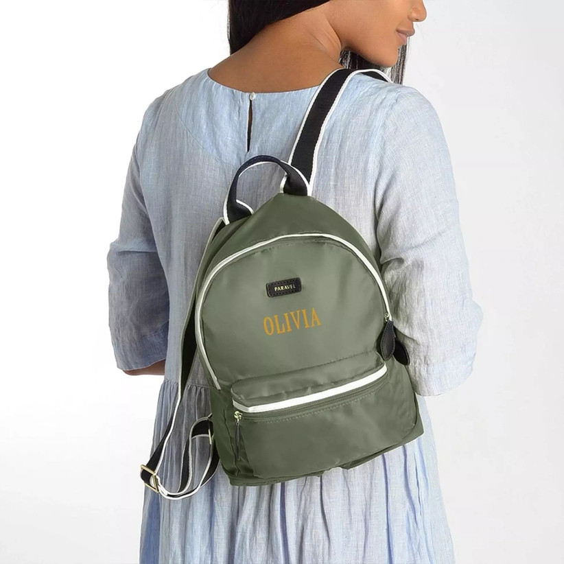 Woman carrying small green backpack personalized with her name in yellow and with black straps