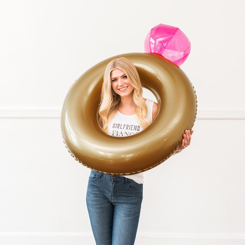 Woman smiling holding giant inflatable diamond ring with her head through the hole