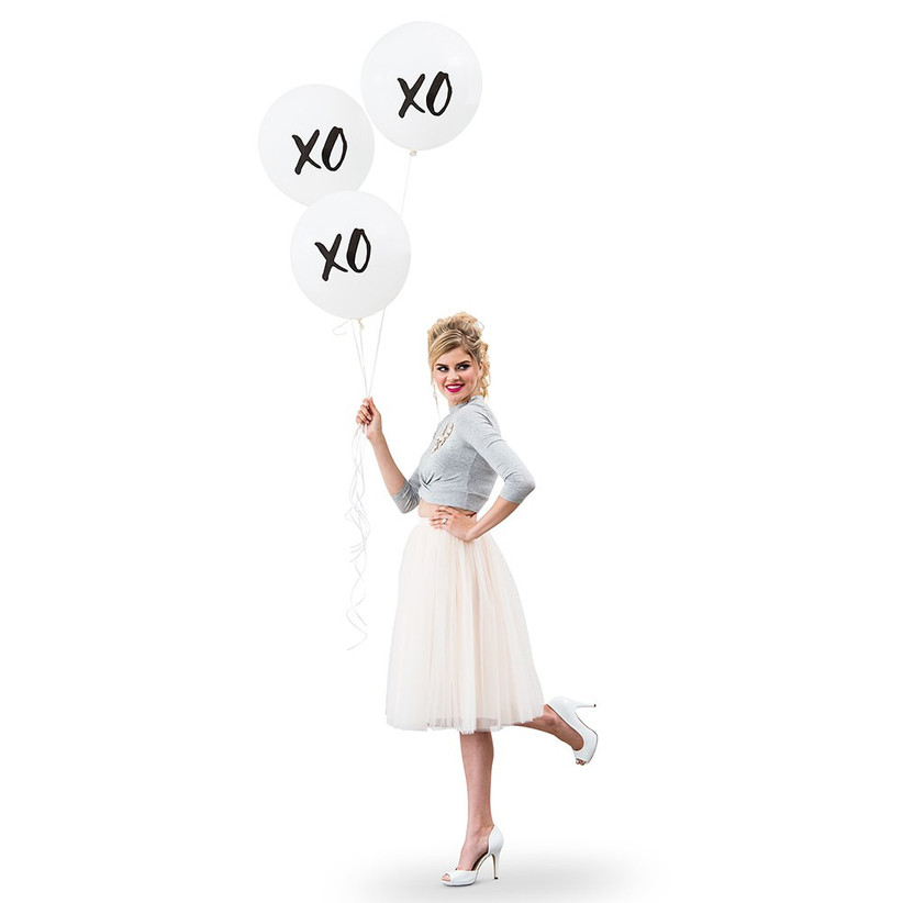 Woman smiling holding three large XO balloons against a white backdrop
