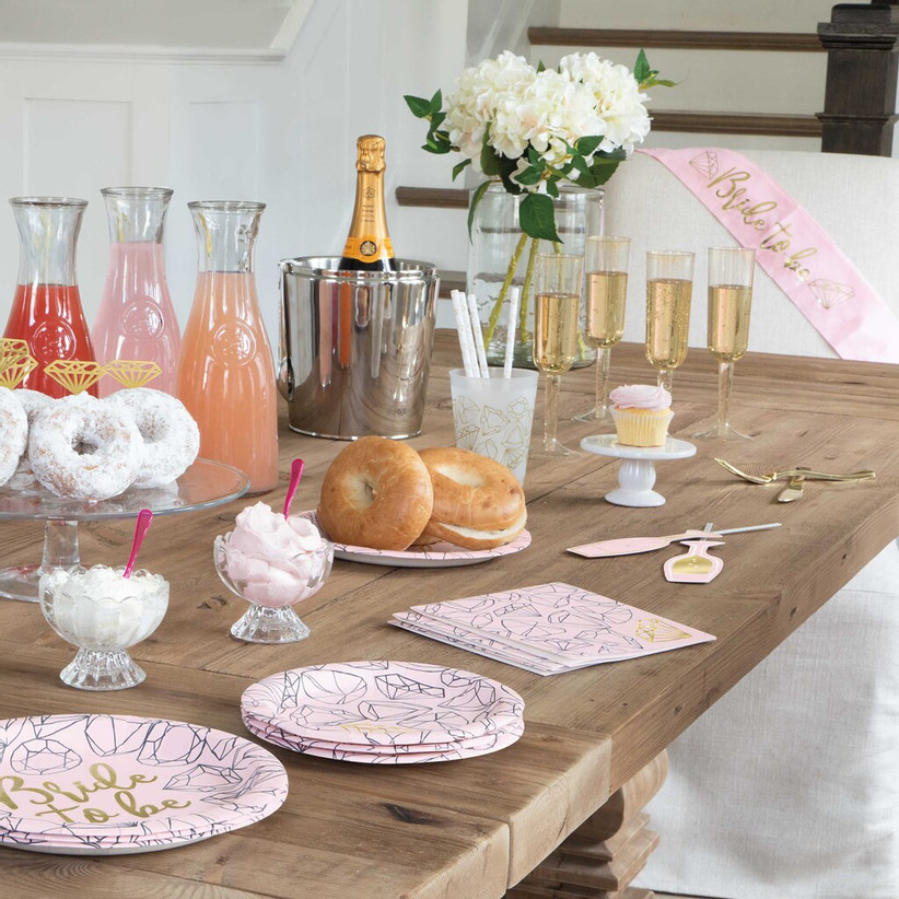 Celebratory bachelorette party table spread with drinks, champagne, donuts, and diamond-patterned paper plates and napkins