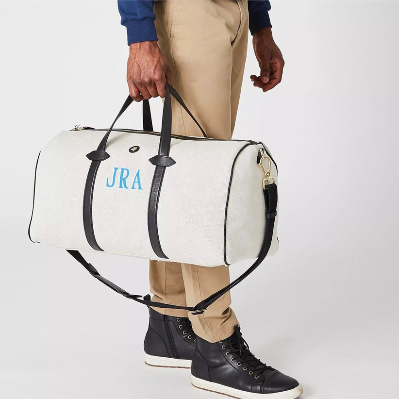 Close up of man holding black and white duffel bag with his initials in blue