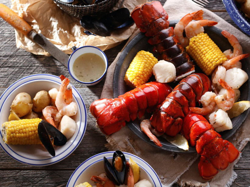 dinner spread featuring lobster, corn on the cob, mussels, scallops