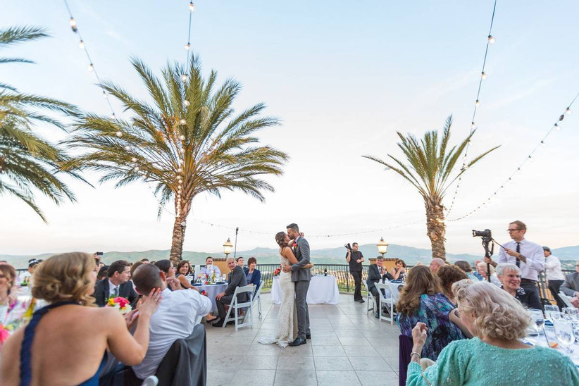пара целуется во время первого танца во время приема на открытом воздухе в окружении пальм