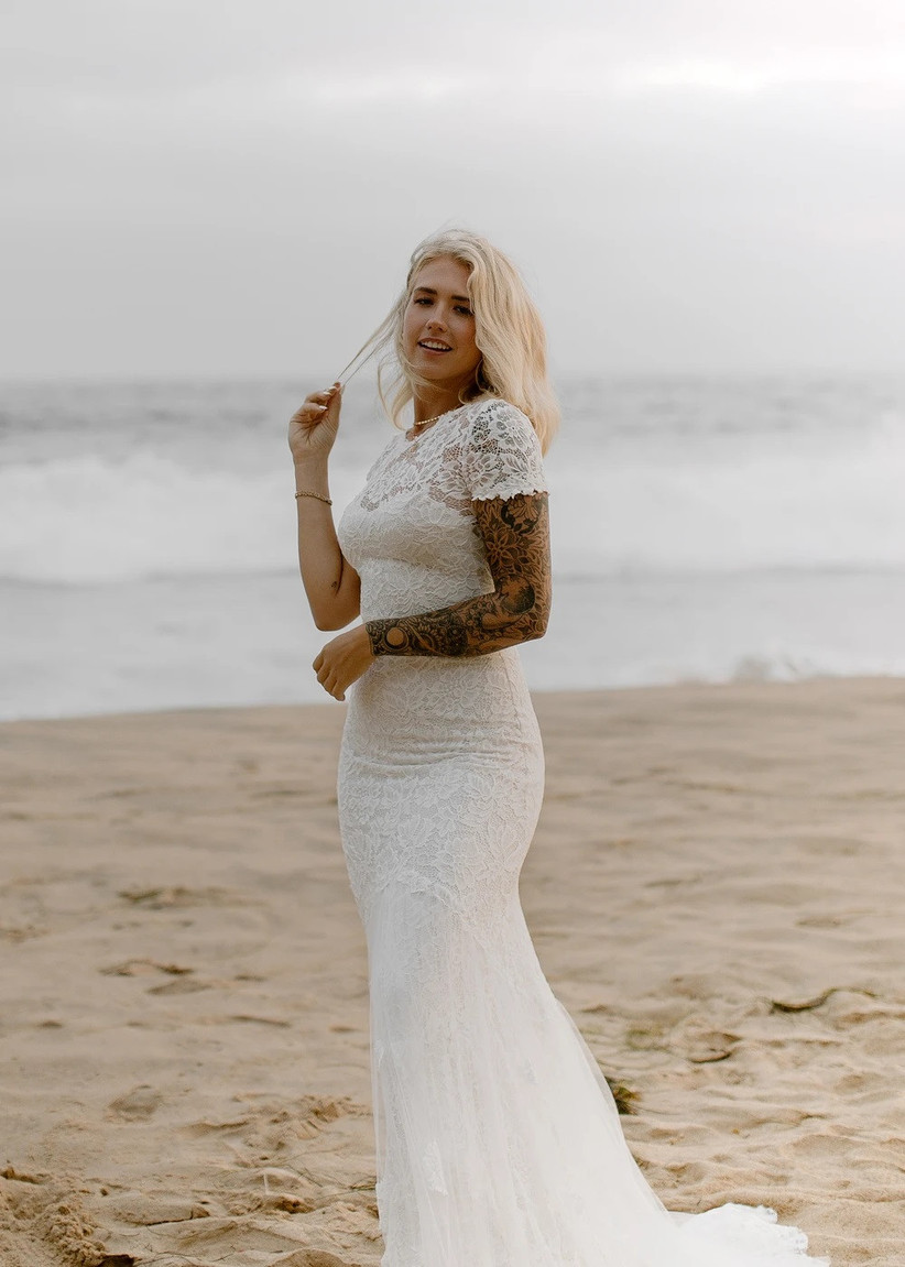 Model wearing fitted lacy wedding gown with short sleeves on the beach