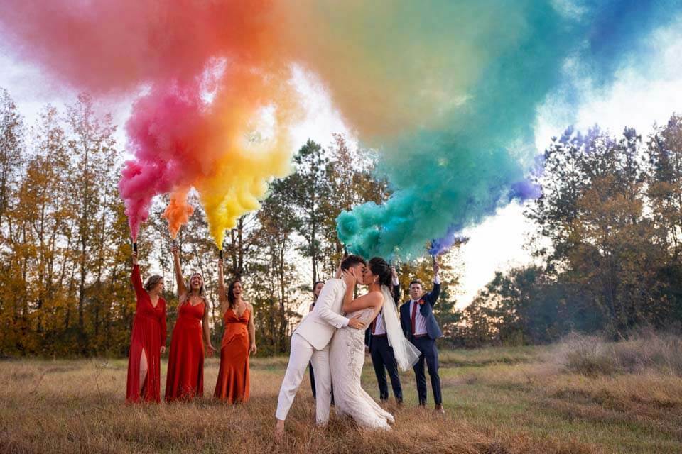 Две невесты целуются, когда их свадебная вечеринка запускает радужное облако дымовых шашек