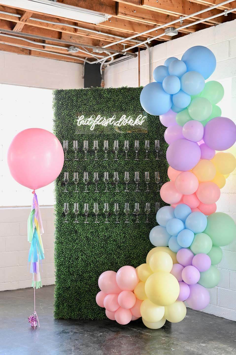 Пастельная радужная инсталляция с воздушным шаром украшает зеленую стену из шампанского