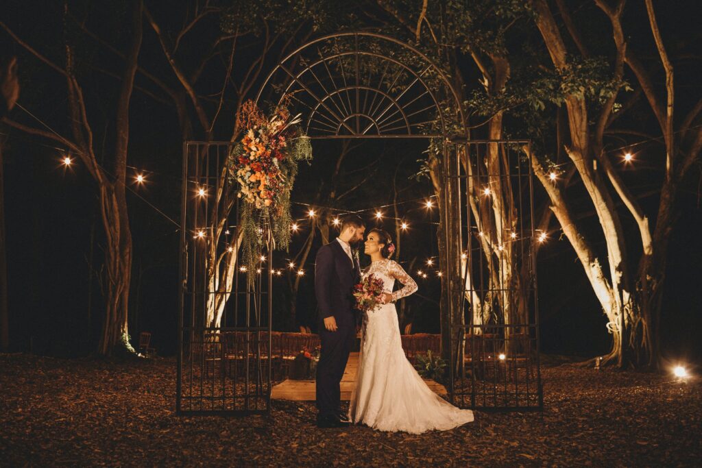 Молодожены фотографируются на свадьбе под открытым небом, освещенной фонарями. 