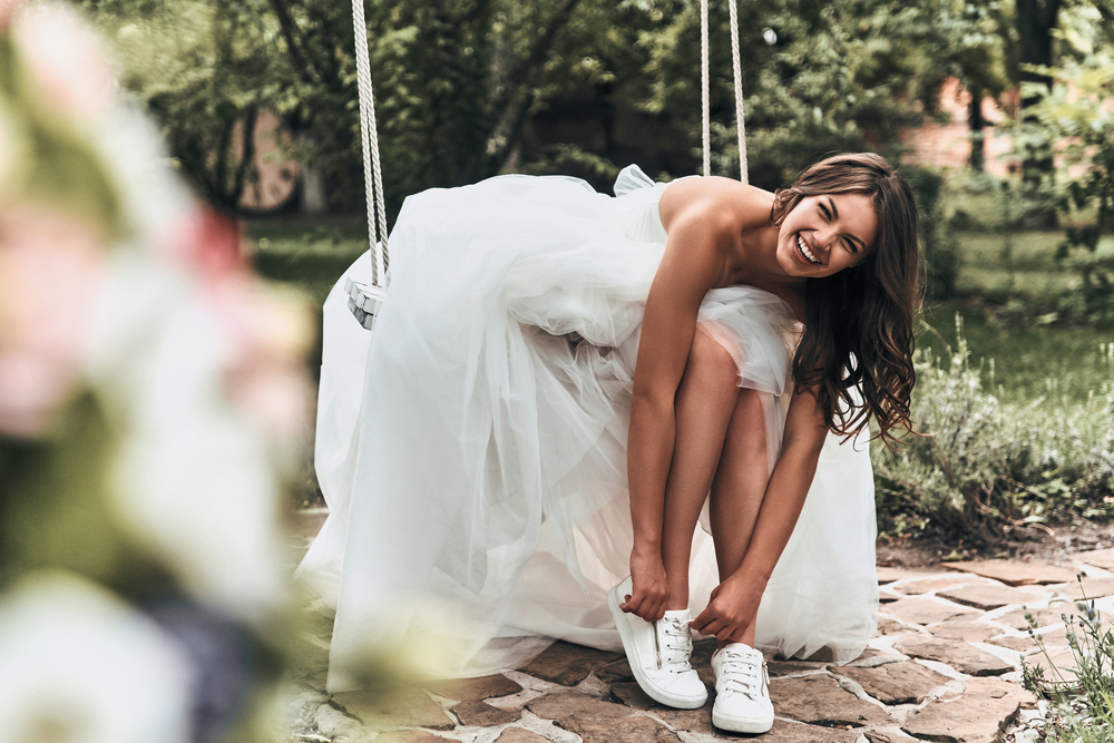 Невеста меняет высокие каблуки на кроссовки во время свадьбы под открытым небом. 